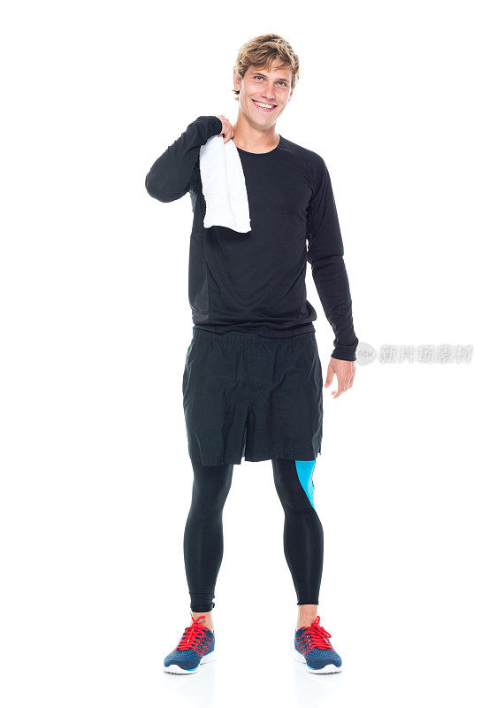 全身长度20-29岁英俊的人白人男性/年轻男子运动员/运动员站在白色背景前，穿着运动服/ t恤/跑步短裤/短裤/连裤袜/打底裤，拿着或穿着毛巾